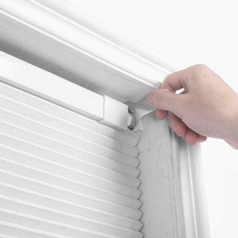 A hand installing Berissa Classic No Drill Blackout Honeycomb Cellular Shades in a window frame.