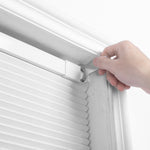 A hand installing Berissa Classic No Drill Blackout Honeycomb Cellular Shades in a window frame.